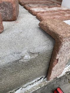 a red toy car is parked on the concrete steps next to some bricks and cement blocks