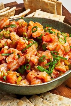 a bowl filled with shrimp and veggies next to crackers