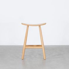 a wooden stool sitting on top of a cement floor next to a white wall in an empty room