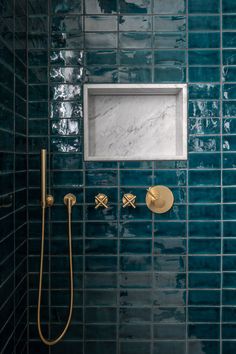 a blue tiled bathroom with gold fixtures and a square mirror on the wall above the faucet