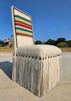 an upholstered chair with fringes and buttons on the back is shown in front of a blue sky