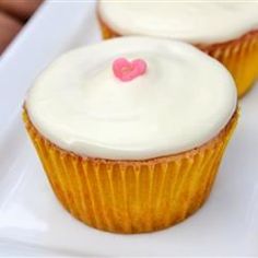 two cupcakes with white frosting and a pink heart on top are sitting on a plate