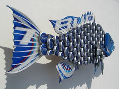 a blue and white fish made out of soda cans on a white surface with shadow