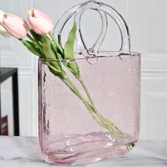 pink flowers are in a clear vase on a marble countertop with white walls and doors