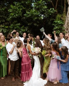 a group of people standing next to each other in front of trees and bushes holding flowers