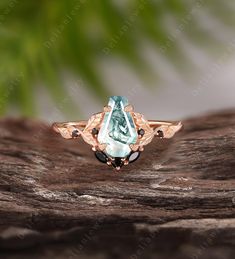 an aqua and black diamond ring sitting on top of a piece of wood with leaves in the background