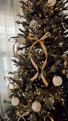 a decorated christmas tree with gold ribbon and ornaments on it's top, in front of a window