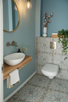 a white toilet sitting next to a sink in a bathroom under a large round mirror