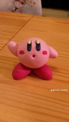 a pink toy sitting on top of a wooden table next to a white object with black eyes