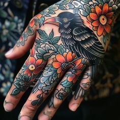 a person's hand with tattoos on it and a black bird sitting on top of flowers