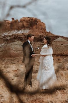 a bride and groom standing in the desert holding each other's hands as they look at each other