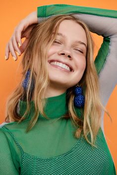 a woman with blonde hair and blue earrings smiles at the camera while leaning on an orange background