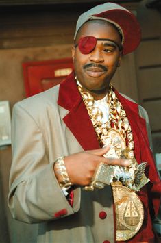 a man in a suit and red hat with gold jewelry on his chest, holding onto a coin