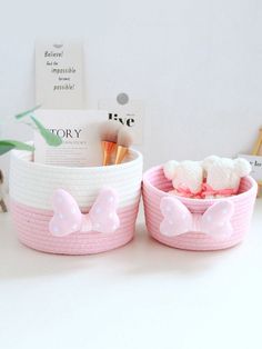 two pink baskets with white bows on them and toothbrushes in the bottom one