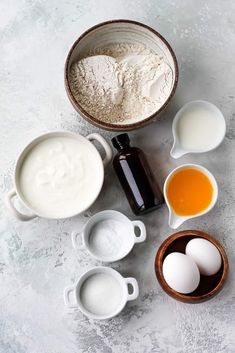 an assortment of ingredients including eggs, milk and flour in bowls on a white surface