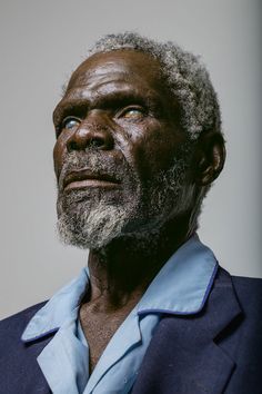 an older man with white hair and beard wearing a blue shirt looks up at the sky