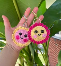 two crocheted keychains with faces on them in front of a plant