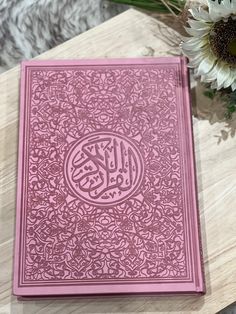 a pink book sitting on top of a wooden table next to a vase with flowers