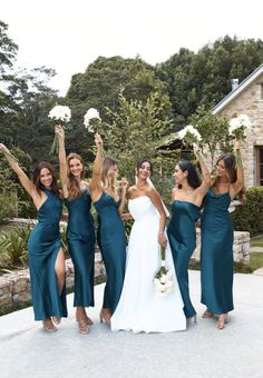 a group of women standing next to each other in front of a stone building holding bouquets