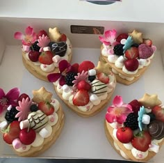 four heart shaped cakes decorated with fruit and flowers on top of a white countertop