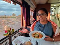 a woman holding a plate of food in front of a window on a train with desert scenery