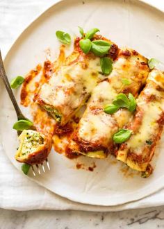 a white plate topped with lasagna covered in sauce and cheese next to a fork