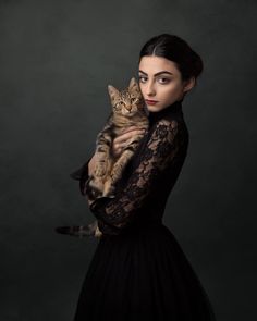 a woman in a black dress holding a cat up to her chest and looking at the camera