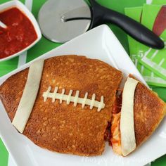 a football cut in half sitting on top of a white plate next to sauces