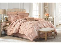 a bed with pink comforter and pillows in a room next to a chair, table and lamp