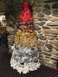 three different colors of paper flowers in front of a stone wall with a sign on it