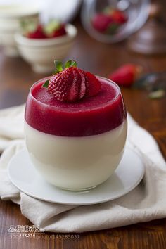 a dessert with strawberries on top is sitting on a white plate and sits on a wooden table