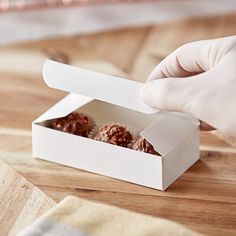 a person in white gloved hands reaching into a box filled with donuts on top of a wooden table