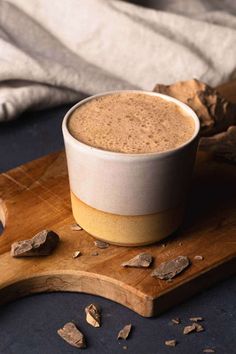 a cup of coffee sitting on top of a wooden cutting board next to some rocks