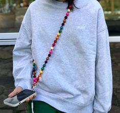 a person with a cell phone and beaded necklace on their neck is standing outside