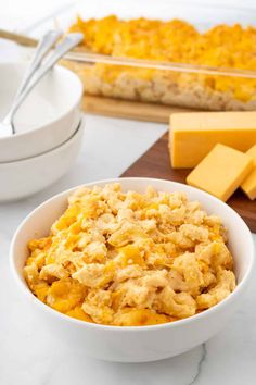 a bowl filled with macaroni and cheese on top of a white counter next to a wooden cutting board