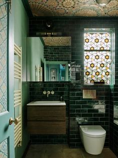 a bathroom with green walls and tiled flooring next to a white toilet sitting under a window