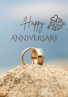 two wedding rings sitting on top of a sandy hill with the words happy anniversary written in black