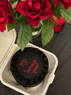 there is a black cake with red writing on it and roses in the vase behind it