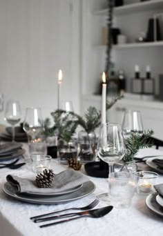 the table is set for christmas dinner with candles and pine cone centerpieces on it