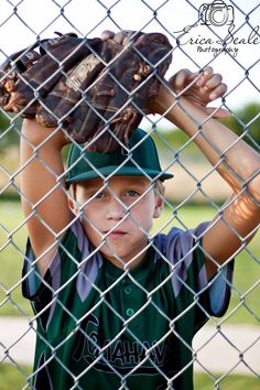 a young boy wearing a catchers mitt on top of his head behind a chain link fence