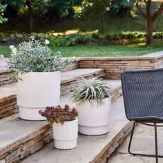 three white planters sitting on the steps in front of a stone wall and lawn