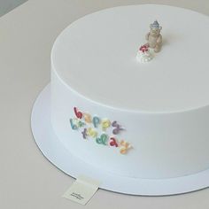 a white cake with letters and a bear figurine on top