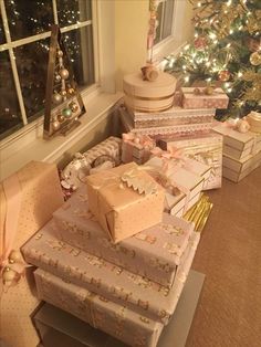 many presents are piled up in front of a christmas tree with lights on the windowsill