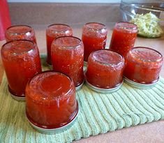 there are many jars with red liquid in them on the table next to some food