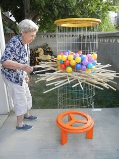 an older woman standing in front of a basket filled with sticks and balls on top of a table