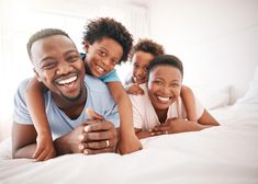 a man, woman and child laying on top of a bed smiling at the camera