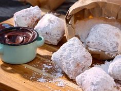 powdered sugar covered pastries are on a cutting board with a cup of chocolate