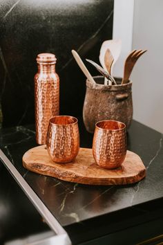 three copper cups sitting on top of a wooden tray