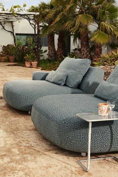 a blue couch sitting on top of a cement floor next to palm trees and potted plants