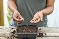 a man holding soil in his hands while standing next to a container filled with dirt